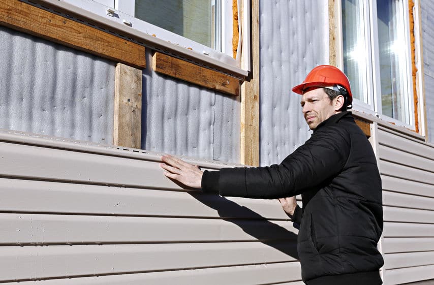 A worker installs panels beige siding on the facade of the house